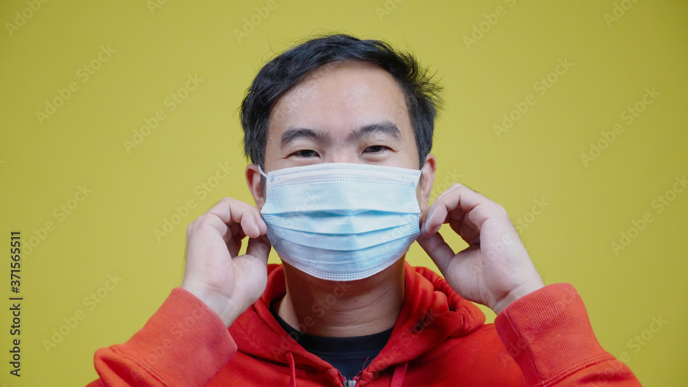 Portrait happy Asian man wear face mask to protect against Coronavirus (COVID-19) or bacteria and dust. Face Authentic close up. isolated Yellow on background. Concept Health care Portrait happy Asian man wear face mask to protect against Coronavirus (COVID-19) or bacteria and dust. Face Authentic close up. isolated Yellow on background. Concept Health care