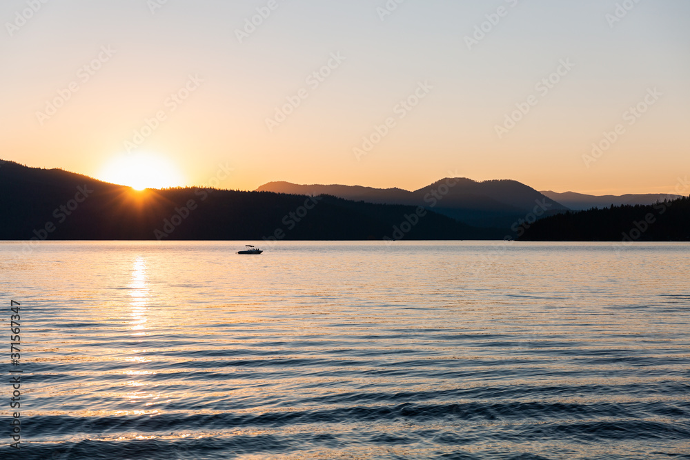 sunset behind silhouetted mountains on a lake with a boat and waves sunset behind silhouetted mountains on a lake with a boat and waves