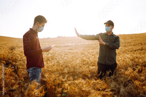 Farmers in a sterile mask with a tablet in their hands in a wheat field. Agro business. Agriculture and harvesting concept.