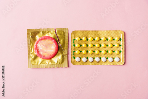 World sexual health or Aids day, condom on wrapper pack and contraceptive pills blister hormonal birth control pills, studio shot isolated on pink background, Safe sex and reproductive health concept