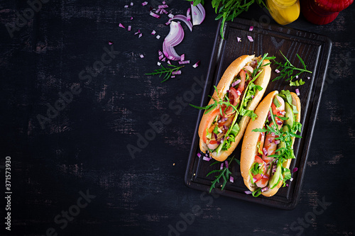Hot dog with sausage, cucumber, tomato and red onion on dark background. Top view. Flat lay. Copy space