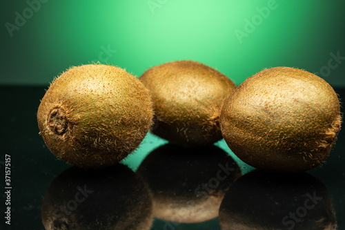 several kiwis on dark glass with green glare on green background