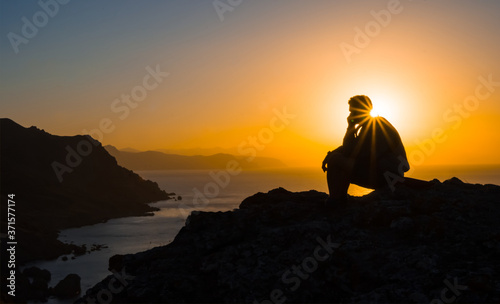 man silhouette sitting on a sea cape at the sunset