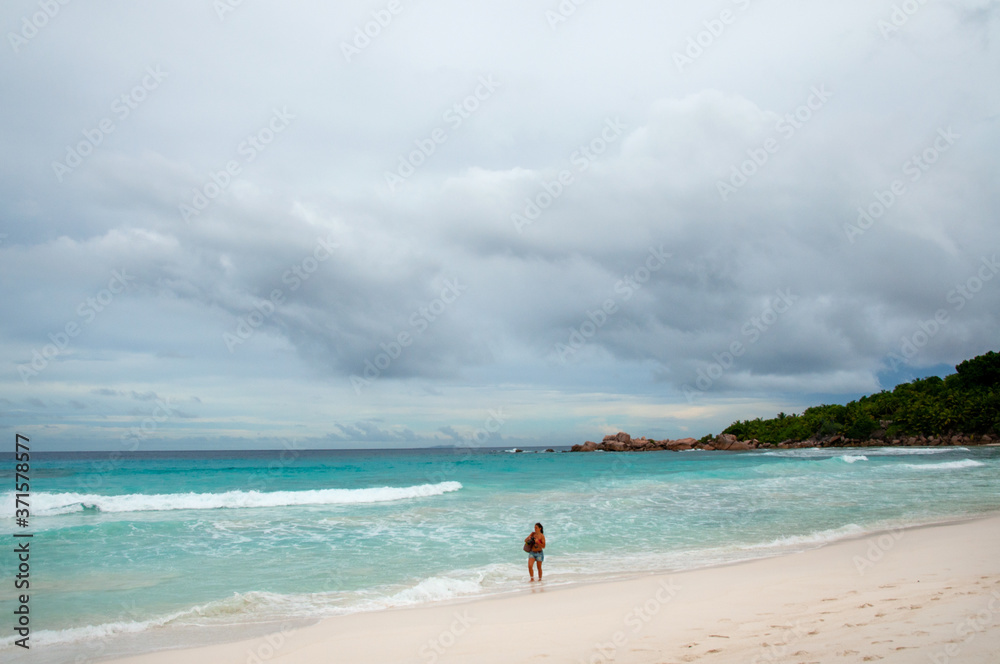 Sandy beach scenic view at the bay of Anse Cocos with one person walking on the shore. La Digue Island, Seychelles