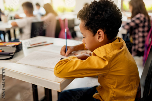Fotografia, Obraz African American schoolboy writing at his desk in the classroom.