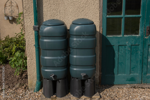 Two Green Water Butts Collecting Rain Water from a Down Pipe by a Building in Rural Devon, England, UK