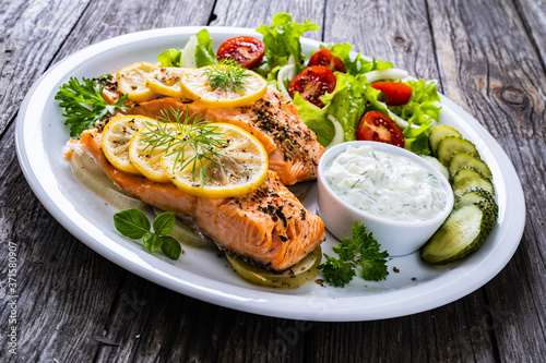 Roasted salmon steaks with lemon, cream sauce and vegetable salad served on wooden table 