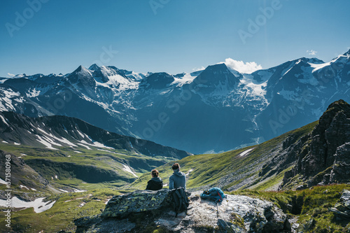 Two hikers sitting on the top of a mountain, relaxing and enjoying a scenic view © Pavlo Glazkov
