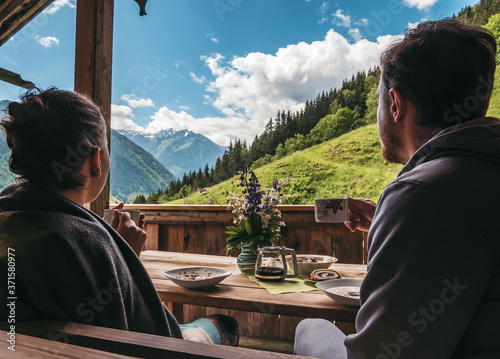 Photography Couple sitting outside of a mountain hut, eating breakfast and enjoying the scen