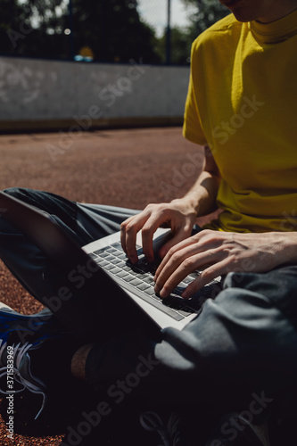 Person sits in a lotus position and holds a laptop on his feet. A man is typing text on a computer keyboard with his hands. Work on the street.