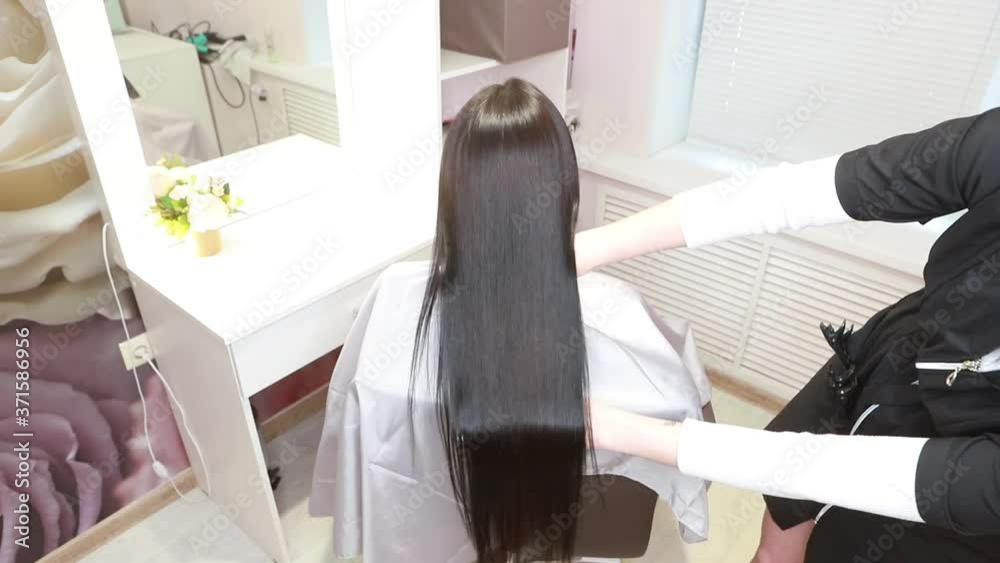 A hairdresser demonstrates the result after lamination and straightening of hair in a beauty salon for a girl with brown hair. hair care concept. Keratin hair treatment