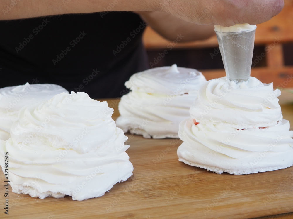 the pastry chef squeezes cream on the cakes. cream on meringue. preparation of dessert. the pastry chef squeezes cream on the cakes. cream on meringue. preparation of dessert.