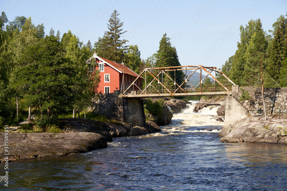 Old red building with a rusty metal bridge over a mountain river in Telemark, Norway