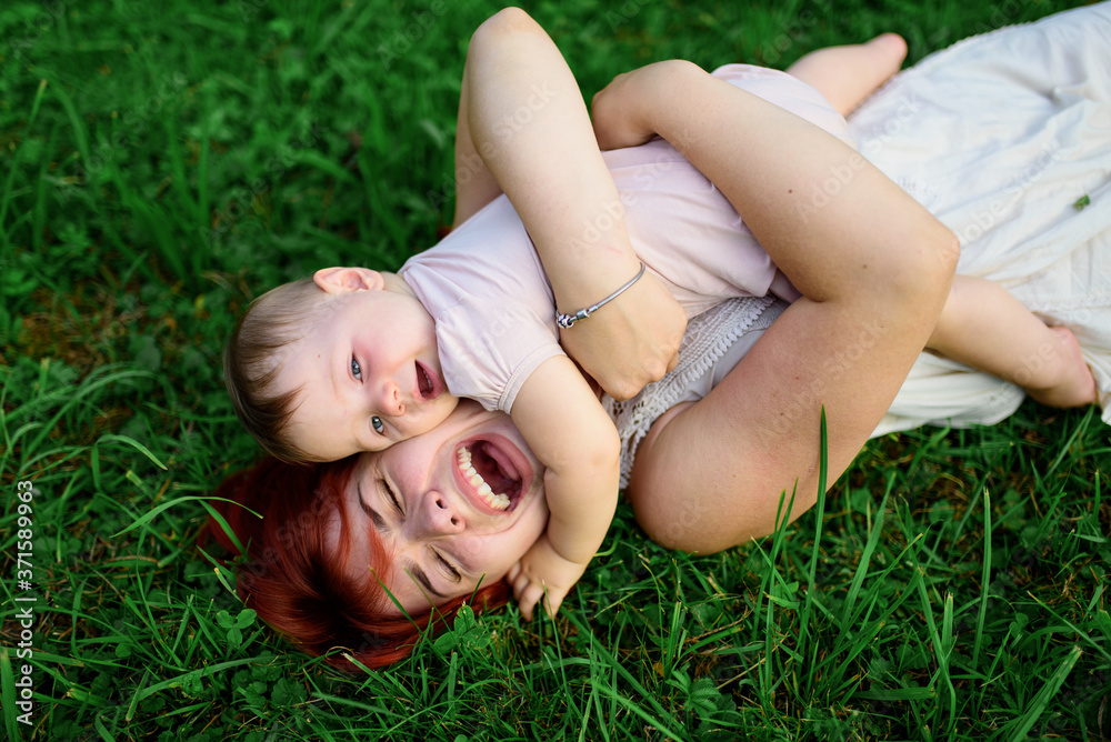 Mom and her one-year-old daughter are hugging on the grass in the park. Mom and her one-year-old daughter are hugging on the grass in the park.