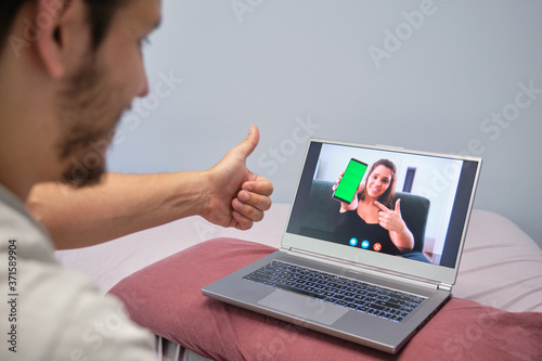 Young man thumbs ups, talking with a young woman who is showing something to him on her phone. Young couple online call concept.
