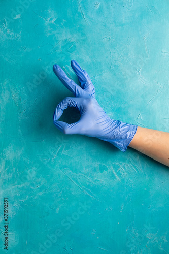 Covid-19 prevention. Pandemic hygiene. Hand in protective gloves showing Ok gesture on textured blue. Quarantine restriction. Medical help