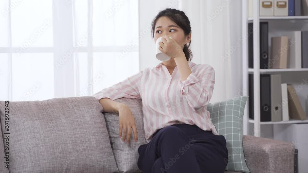 asian professional woman sitting and leaning on back of the sofa is relaxing and enjoying hot tea. chinese female ceo noticing notification on phone and taking a look at it. asian professional woman sitting and leaning on back of the sofa is relaxing and enjoying hot tea. chinese female ceo noticing notification on phone and taking a look at it.