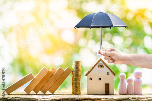 Obraz na plátně Collect gold coin and woman hand hold open the black umbrella for protect the home and family from hazard falling wood block in the public park, Saving money for buy insurance of real estate concept