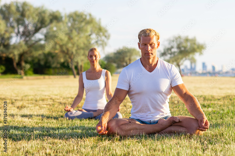 Fototapeta premium Fit man and beautiful woman practicing yoga outdoor on the grass. Stretching exercise in the sunset. Sport, fitness, health care and lifestyle concepts.
