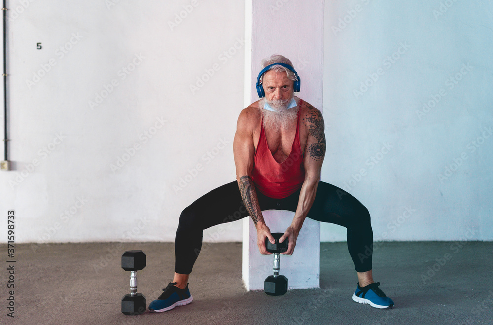 Senior man doing gym workout with dumbbells while wearing face protective mask during Coronavirus isolation quarantine - Fitness, sport and healthy elderly lifestyle - Focus on face Senior man doing gym workout with dumbbells while wearing face protective mask during Coronavirus isolation quarantine - Fitness, sport and healthy elderly lifestyle - Focus on face