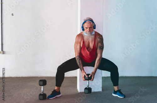 Senior man doing gym workout with dumbbells while wearing face protective mask during Coronavirus isolation quarantine - Fitness, sport and healthy elderly lifestyle - Focus on face