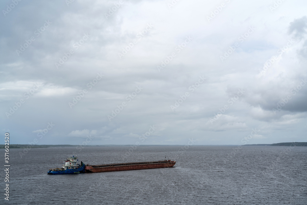 The barge floats down the river on a cloudy day. Transportation of goods by water.