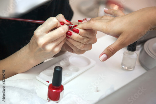 Gel polish design. Female master in the salon is painting with brush on the hands of the client. Beauty industry, creativity concept