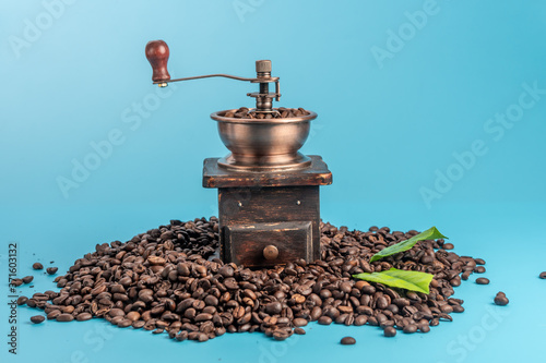 Vintage style coffee grinder and roasted coffee beans on a blue background