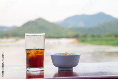 Cola in glass and bowl contain beans on table with mountain and river background