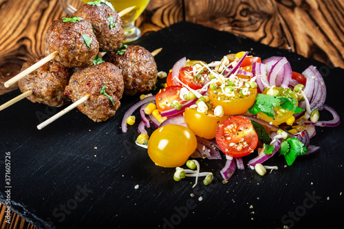 Lula kebab from lamb on a wooden skewer with a salad from Cherry tomatoes, red onions and green beans. Slate plate on a wooden background. Selective focus.
