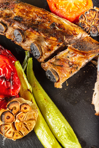 Pork ribs and vegetables on a cast iron pan. Wooden background. Close up. Selective focus.