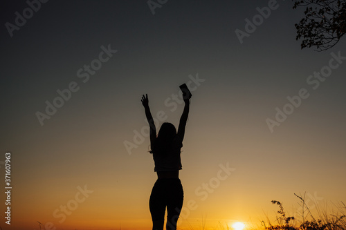 The girl at sunset. She stands back to the camera on the top of the mountain and looks at the sunset, welcomes the sun with her hands up. Girl listen the music. Copy space.