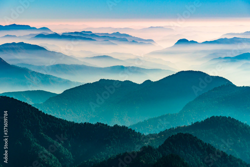 View of Himalayas mountain range with visible silhouettes through the colorful fog from Khalia top trek trail. Khalia top in himalayan region of Kumaon, Uttarakhand, India.