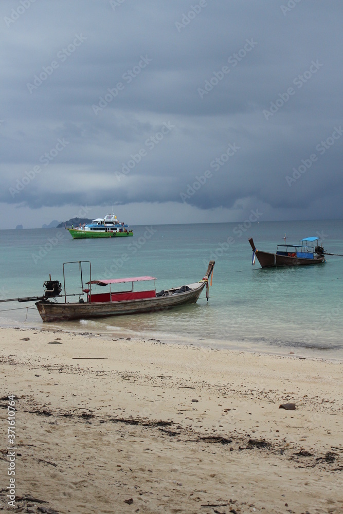 long tale boats at a turquoise beach and cloudy sky