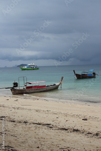 long tale boats at a turquoise beach and cloudy sky