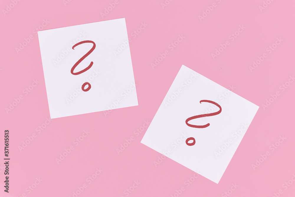 White sticky notes with handwritten question mark symbol in red ink on pink background White sticky notes with handwritten question mark symbol in red ink on pink background