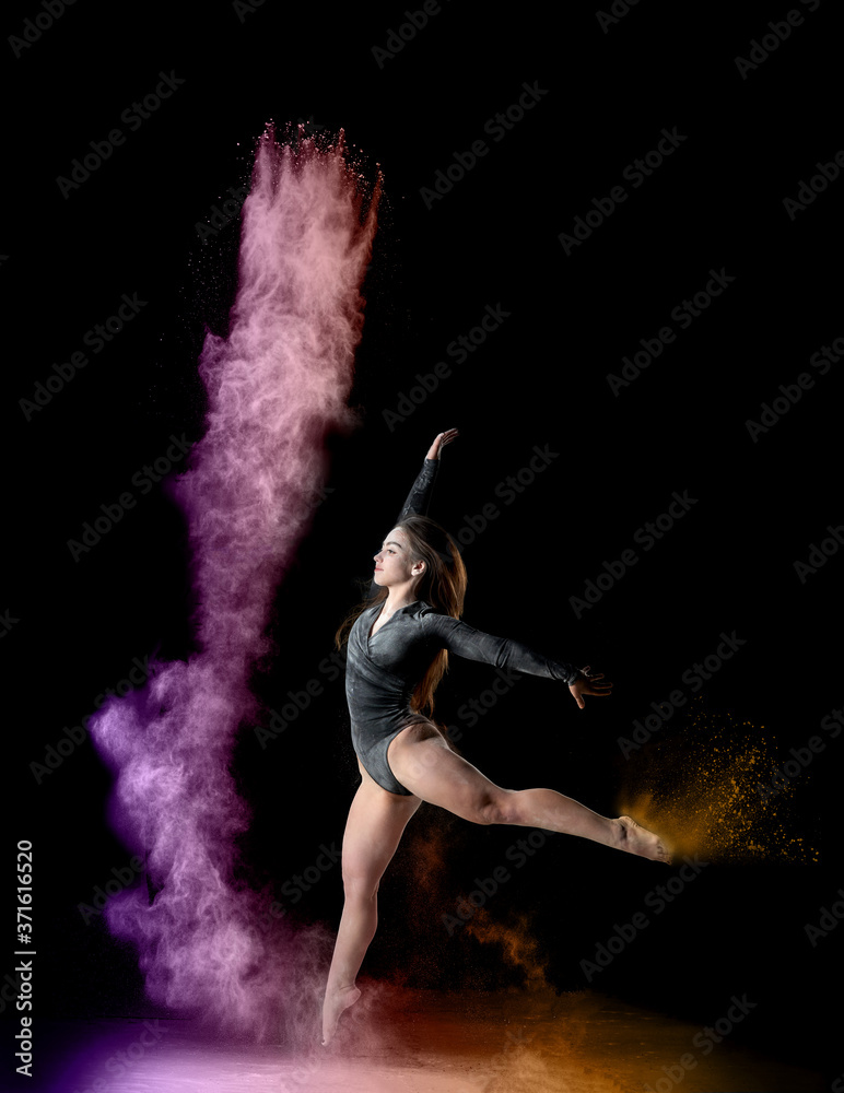 beautiful young caucasian woman in a black bodysuit with a sports figure dancing in a purple-yellow cloud of flour