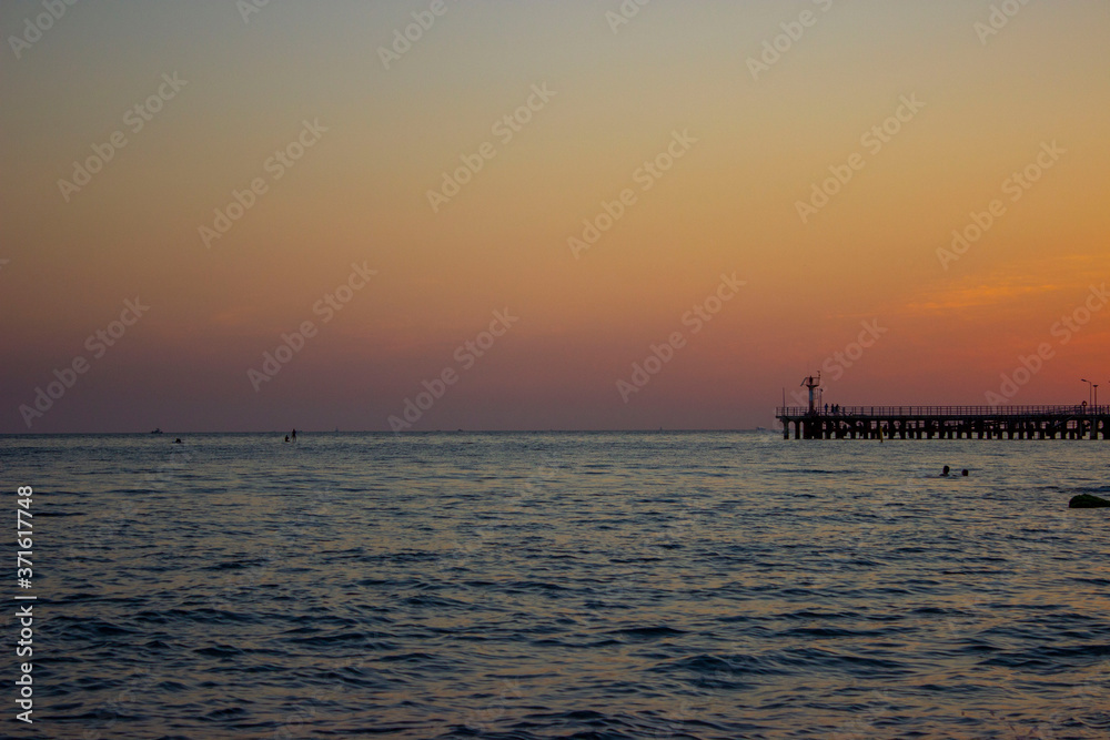 Gentle sunset, yellow pink. Blue dark gray color of the sky and sea. The silhouette of the pier is visible. The sun has just set.