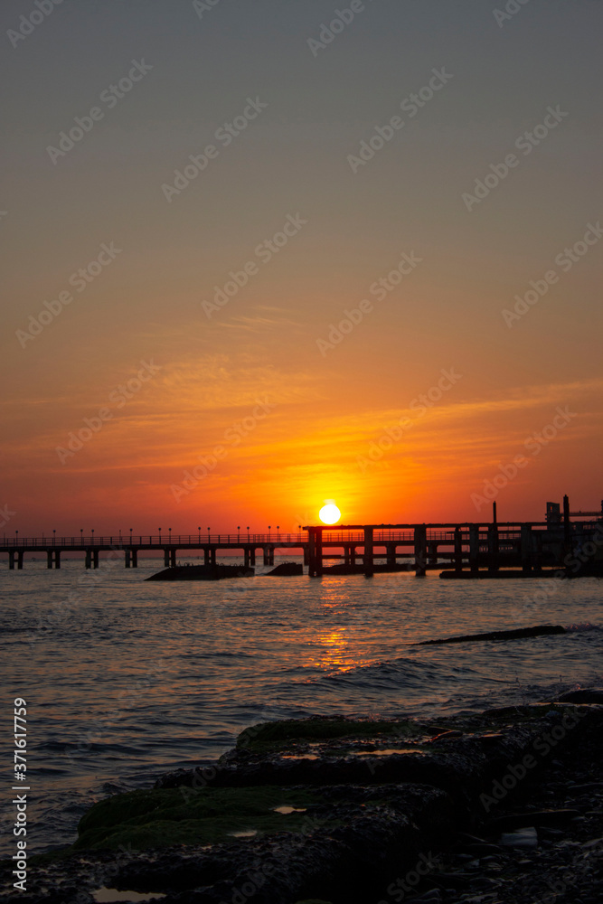 Bright orange red sunset on the sea. The silhouette of the pier goes into the distance. concrete slabs and breakwaters are visible. Everything is illuminated by the light of the departing sun.
