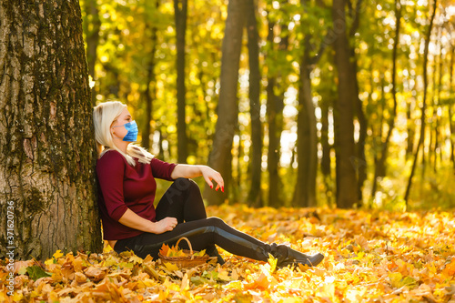 Autumn portrait of a young woman in a medical mask and glasses. Girl close-up on the background of yellow leaves, copy space.