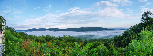 panorama of senior female photographer making pictures of fog in the valley below a scenic overlook along the skyway motorway in the talladega national forest, alabama, usa photo