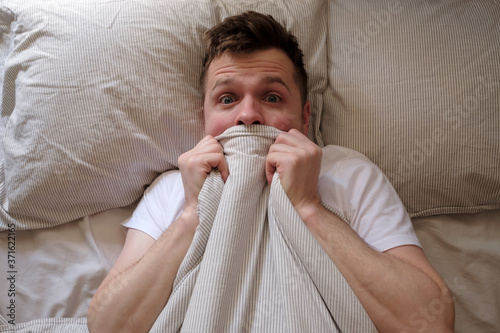Man hiding in bed under the blanket at home