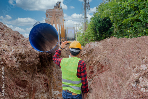 A young Asian engineer is inspecting a large sewer that is buried underground at a construction site. The excavator is empty the water pipe. photo