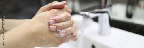 Close-up of person washing hand with soap. Bathroom with water pouring out of crane. Prevention of infection and virus. Personal hygiene and cleanliness concept
