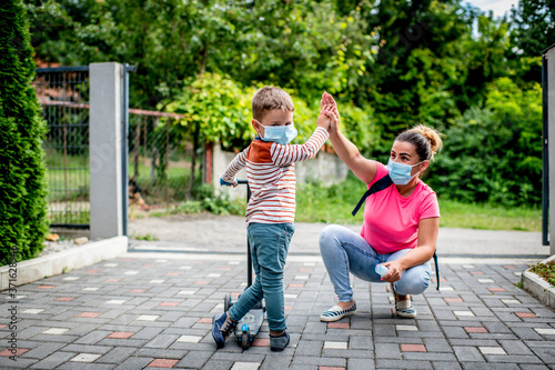 Mother and son with protective masks riding scooter in a front of backyard