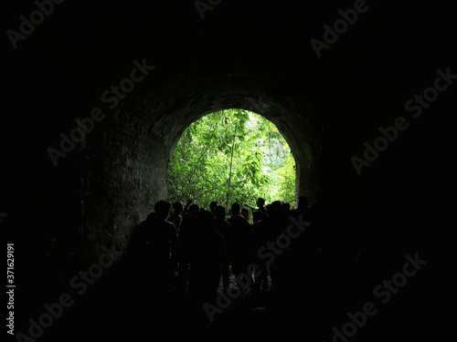 group of people standing in the light at the end of a tunnel, in a forest. Old train of Venezuela.