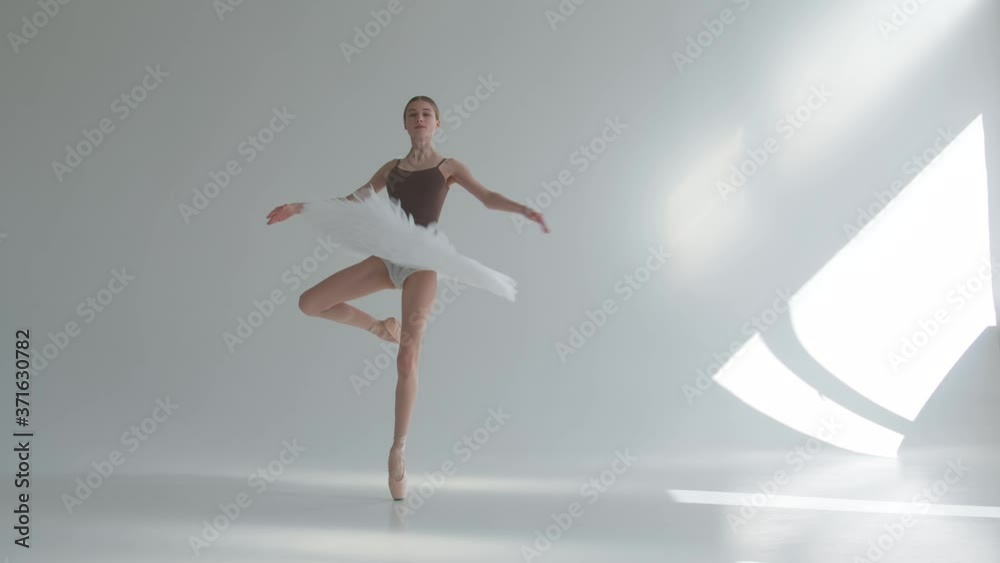 Young ballerina in pointe shoes and white ballet tutu makes pirouette. Shot on a white background in the spacious and brightly lit studio.