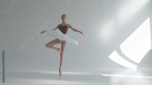 Young ballerina in pointe shoes and white ballet tutu makes pirouette. Shot on a white background in the spacious and brightly lit studio.