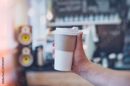 Mock-up of a cardboard glass for coffee in a guy's hand against the background of a bar in a cafe.
