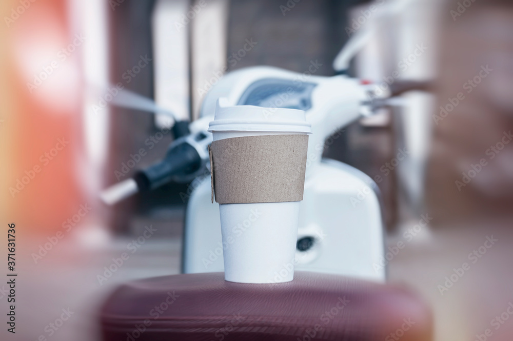 A man holds an ecological cup with coffee in his hand. Mock up paper cup on the background of a motor scooter. A man holds an ecological cup with coffee in his hand. Mock up paper cup on the background of a motor scooter.